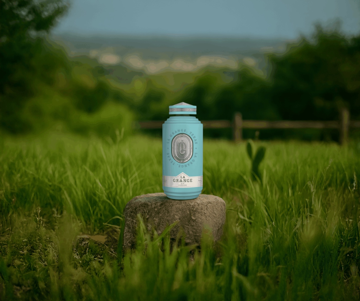 La Grange Verdure gin bottle on a stone in a green pasture with a ranch fence behind