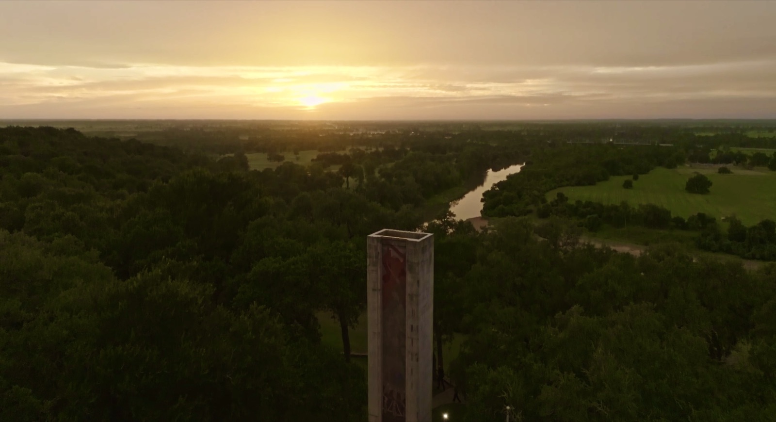 Aerial view at sunset of the Monument Hill tower above the trees, with the Colorado River bending through the plain below